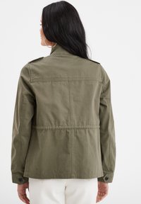 Giacca in cotone verde oliva con colletto alla cinese. Presenta spalline e polsini regolabili con bottoni. Orlo dritto e cuciture posteriori visibili.