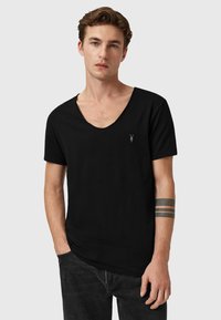 Camiseta de algodón negra con un diseño de escote en V profundo y mangas cortas. Presenta un pequeño logo en el pecho. Textura suave, ajuste casual.