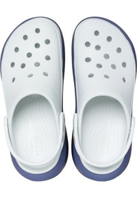 Zuecos de plástico blancos con suelas azules, que presentan múltiples agujeros de ventilación en la parte superior, plantilla con textura y una correa trasera para un ajuste seguro.