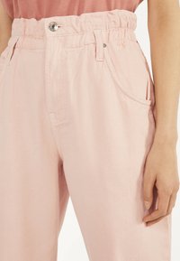 Ljusrosa bomullsbyxor med avslappnad passform, elastisk midja och knappstängning. Har sidofickor och ett mjukt, texturerat tyg.