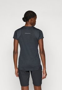 Mørk grå kortermet treningsgenser med rund hals, pustende bakpanel og glidelåslomme på siden. Kombinert med mørke shorts.