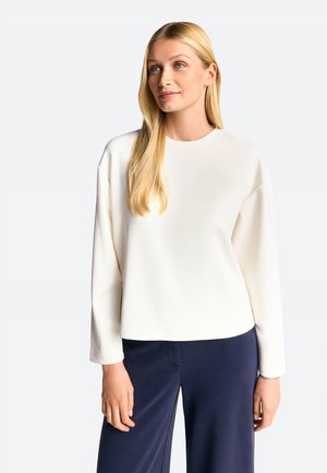 Top a maniche lunghe e collo rotondo in morbido tessuto beige chiaro con una vestibilità rilassata, abbinato a pantaloni blu navy. Design minimalista notevole.