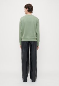 Grønn sweatshirt med rund hals og lange ermer, sammen med svarte vide skinnbukser. Jevn tekstur, minimalistisk design uten synlige logoer.