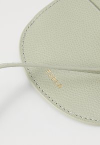 Portafoglio in pelle verde chiaro con superficie testurizzata, bordi arrotondati e logo "FURLA" dorato in rilievo vicino al centro.