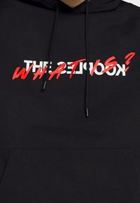 Sudadera negra de mezcla de algodón. Cuenta con un bolsillo tipo canguro y un texto en blanco y rojo que dice "¿LOS KOCKS? ¿QUÉ ES?".