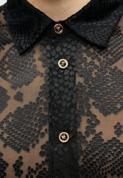 Chemise en tissu noir transparent avec motif à pois texturé, col en velours noir et boutons dorés avec motif en relief.