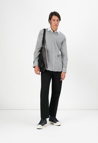 Striped button-up shirt in black and white, paired with black pants and blue sneakers, with a dark bag slung over the shoulder.