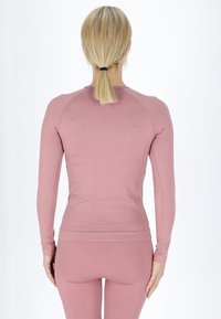Top aderente a maniche lunghe in un tessuto a coste rosa, caratterizzato da un colletto rotondo e spalle senza cuciture, abbinato a leggings a coste dello stesso colore.