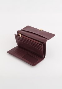 Portfel z bordowej skóry z klapką zamykaną na zatrzask, wieloma miejscami na karty, przedziałem zapinanym na zamek oraz przezroczystym okienkiem na dowód tożsamości. Gładka faktura.