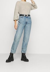 Light gray knitted sweater with wide sleeves, paired with high-waisted blue jeans. Black belt with silver buckle and black combat boots.