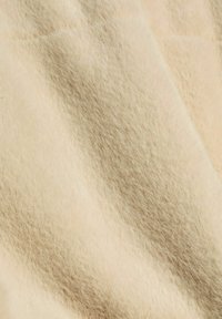Gros plan sur un tissu beige doux avec une texture pelucheuse et duveteuse et un léger ombrage sur la surface.