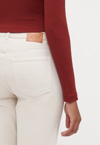 White denim jeans feature a leather "ONLY" label, back pockets with visible stitching, paired with a fitted, long-sleeve red top.