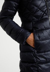 Quilted puffer jacket in dark navy blue, featuring a smooth, shiny texture, zip closure, and side pockets.
