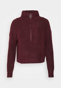 Suéter de punto acanalado burdeos con mangas largas, cuello alto y cremallera frontal con tirador de metal redondo.