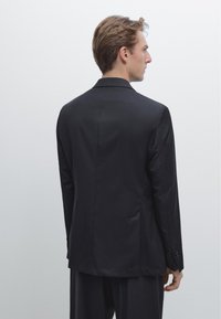 Blazer nero realizzato in tessuto liscio, con un'unica fessura posteriore, rever a punta e polsini con bottoni, dalla vestibilità sartoriale e design minimale.