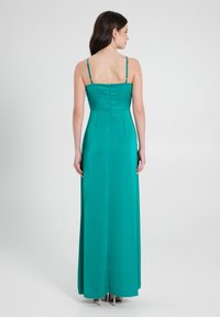 Abito da sera teal con spalline sottili, corpetto aderente e gonna plissettata. Presenta una zip invisibile sul retro e un design lungo fino al pavimento.