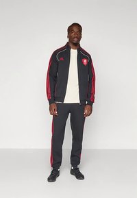 Træningssæt i sort med røde striber, indeholdende en jakke med lynlås og matchende bukser. Fremstillet af åndbart stof og inkluderer logo-detaljer.