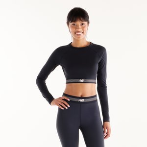 Ung kvinde smilende, stående med hånd på hoften, iført sort langærmet cropped top og matchende høj-taljede leggings med logo bånd.