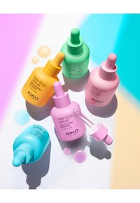 Botellas de suero coloridas con formas redondeadas y tapas de cuentagotas. Los materiales son mates, con etiquetas que indican diversos beneficios para la piel.