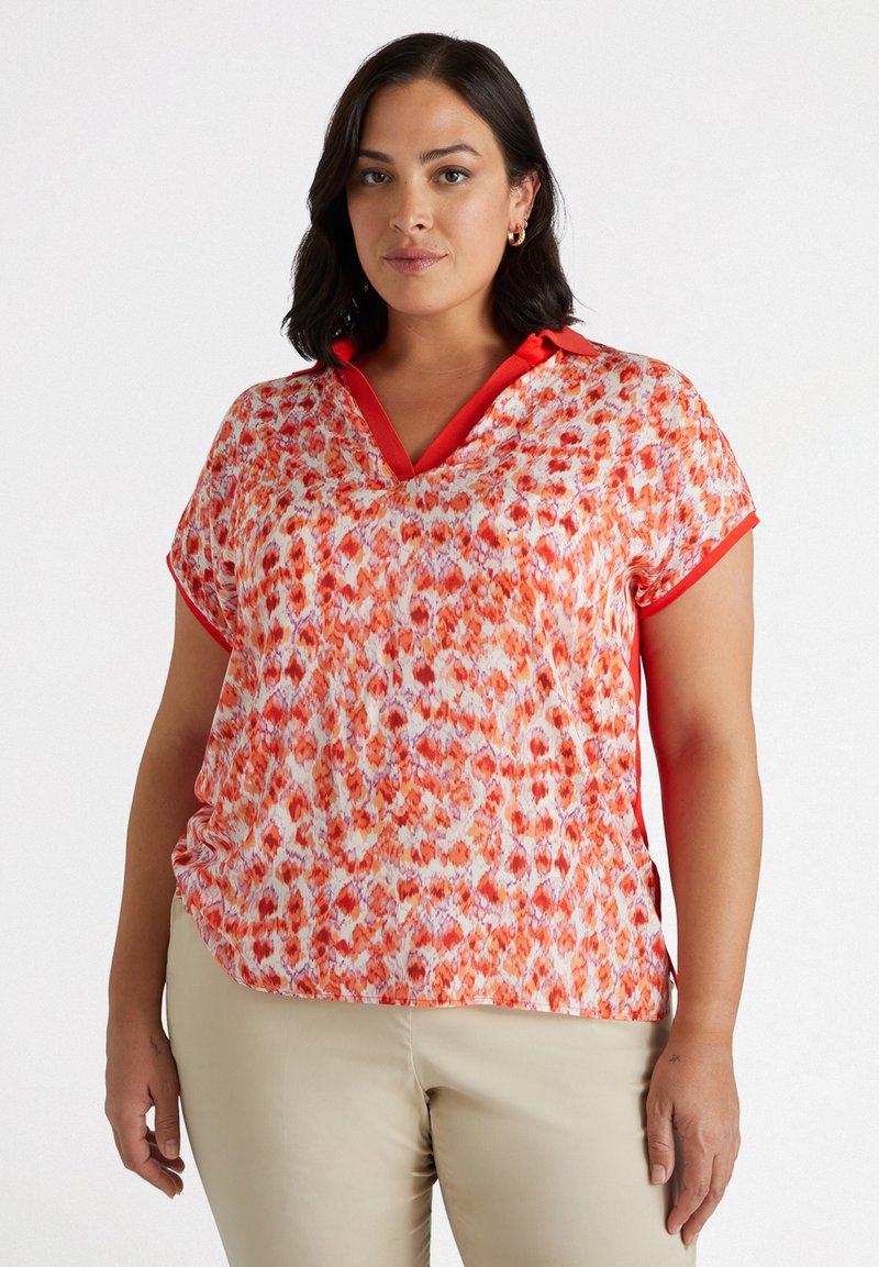 Haut à manches courtes rouge et orange à motifs avec un col en V et un col contrastant. Tissu léger qui tombe doucement, présentant une coupe décontractée.