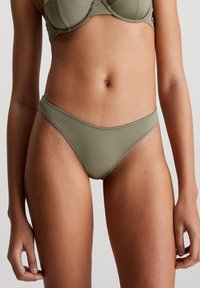 Olivgrön bikiniunderdel med låg midja, slät textur och diskreta sömmar längs midjebandet och benöppningarna.