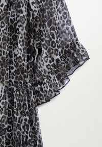 Manche en tissu transparent avec imprimé léopard noir et gris, avec un ourlet à volants et un détail de cordon noué.