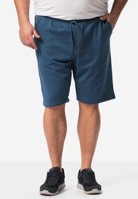 Pantaloni corti in cotone blu con vita elastica e cordoncino, tasche frontali e vestibilità comoda, abbinati a scarpe da ginnastica nere.