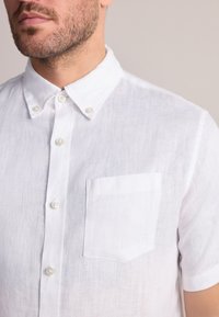 Chemise blanche en lin à manches courtes, dotée d'un col boutonné, de boutons en nacre et d'une poche poitrine avec une finition de couture nette.