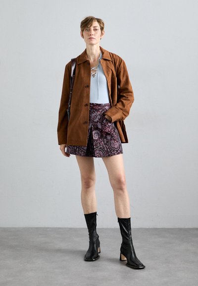Brown suede jacket over a light blue knit top, paired with a patterned purple skirt. Black knee-high boots with a block heel.