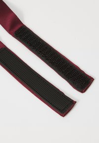 Bordeauxfarbener Stoffriemen mit schwarzem Klettverschluss. Glatte Textur auf einer Seite und eine flauschige Oberfläche auf der anderen Seite.