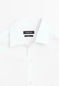 Camicia bianca con colletto classico, caratterizzata da una morbida texture e cuciture visibili. Le etichette includono "Massimo Dutti" e "Made in Cuba."