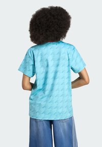 Camisa de manga curta azul clara com um padrão geométrico subtil, detalhe vermelho na gola e um corte descontraído.