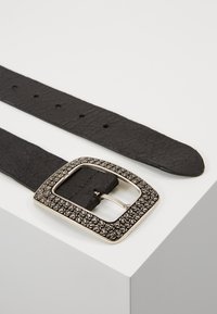 Cintura in pelle nera con superficie testurizzata, caratterizzata da una fibbia decorativa di colore argento con motivi circolari e una forma rettangolare classica.