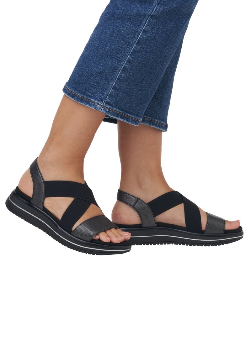 Schwarze und graue Sandalen mit elastischen Riemen, flacher Sohle, strukturiertem Obermaterial und offener Zehenpartie, kombiniert mit Denim-Capris.