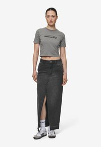 Grå kortärmad t-shirt med svart logotyp, i kombination med en lång svart jeanskjol med en framfåra. Skor: grå sneakers med vita detaljer.