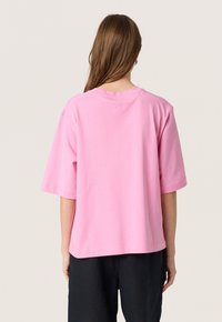 Rosa bomullströja med korta ärmar, en avslappnad passform och rund halsringning. Har en diskret logotyp präglad på baksidan av kragen.