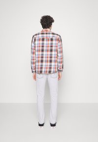 Camicia di flanella a scacchi in diversi colori con motivi arancioni, blu e neri, abbinata a jeans dritti grigio chiaro e sneaker nere.