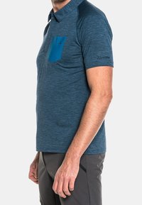 Herrpolo i melerad blått tyg. Har en kontrasterande turkos ficka, korta ärmar och en subtil logodetalj på armen.