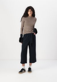 Brown ribbed long-sleeve top with scalloped hem, paired with loose navy culotte pants and black sneakers with white stripes, featuring fuzzy black wrist accents.