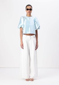 Lyseblå sateng cropped topp med pufferm, kombinert med hvite vide bukser og klare block-heeled sandaler. Sorte solbriller brukt.