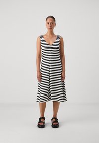 Robe rayée noire et blanche avec un décolleté en V profond, des boutons sur le devant et une silhouette en A, associée à des sandales noires épaisses.
