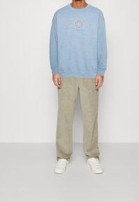 Ljusblå sweatshirt med rund halsringning och subtil grafisk design på bröstet. Matchad med beige kordflorsbyxor och vita sneakers.