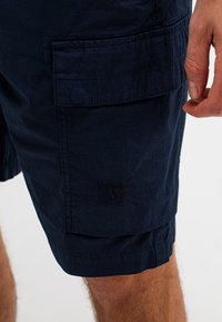 Marineblauwe cargoshorts van katoen, met een zijzak, gestikte details en een klein logopatch op het onderbeen.