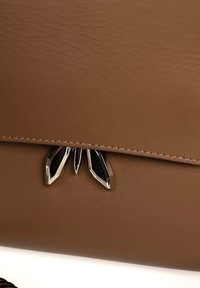 Brun lædertaske med en glat overflade, der har et skinnende sølvfarvet dekorativt hardwareelement, som ligner blade ved lukningen.