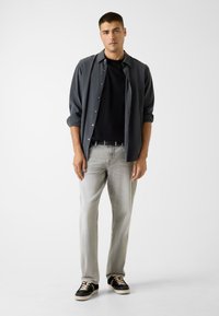 Grijs overhemd over een zwart T-shirt, gecombineerd met lichtgrijze spijkerbroek en zwarte sneakers. Eenvoudig ontwerp met een ontspannen pasvorm.