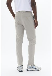 Pantalones gris claro con una textura suave, que presentan dos bolsillos traseros y botones en tono dorado, llevados con calcetines blancos y zapatillas de running plateadas.