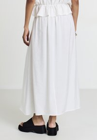 Jupe blanche longueur cheville avec une ceinture élastique froncée, associée à des chaussures à plateforme noires. Tissu doux et léger.