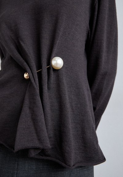 Dark gray sweater featuring twisted fabric detail and a large pearl brooch, secured with a thin gold pin, on the left side.