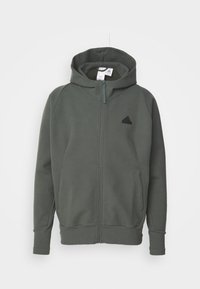 Hoodie zippé vert en tissu doux, avec une fermeture éclair sur le devant, des poches latérales et un logo noir sur la poitrine. Capuche incluse.