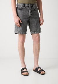 Shorts en denim noir avec une coupe droite, ourlet brut et cinq poches, associés à des sandales noires avec deux brides réglables.